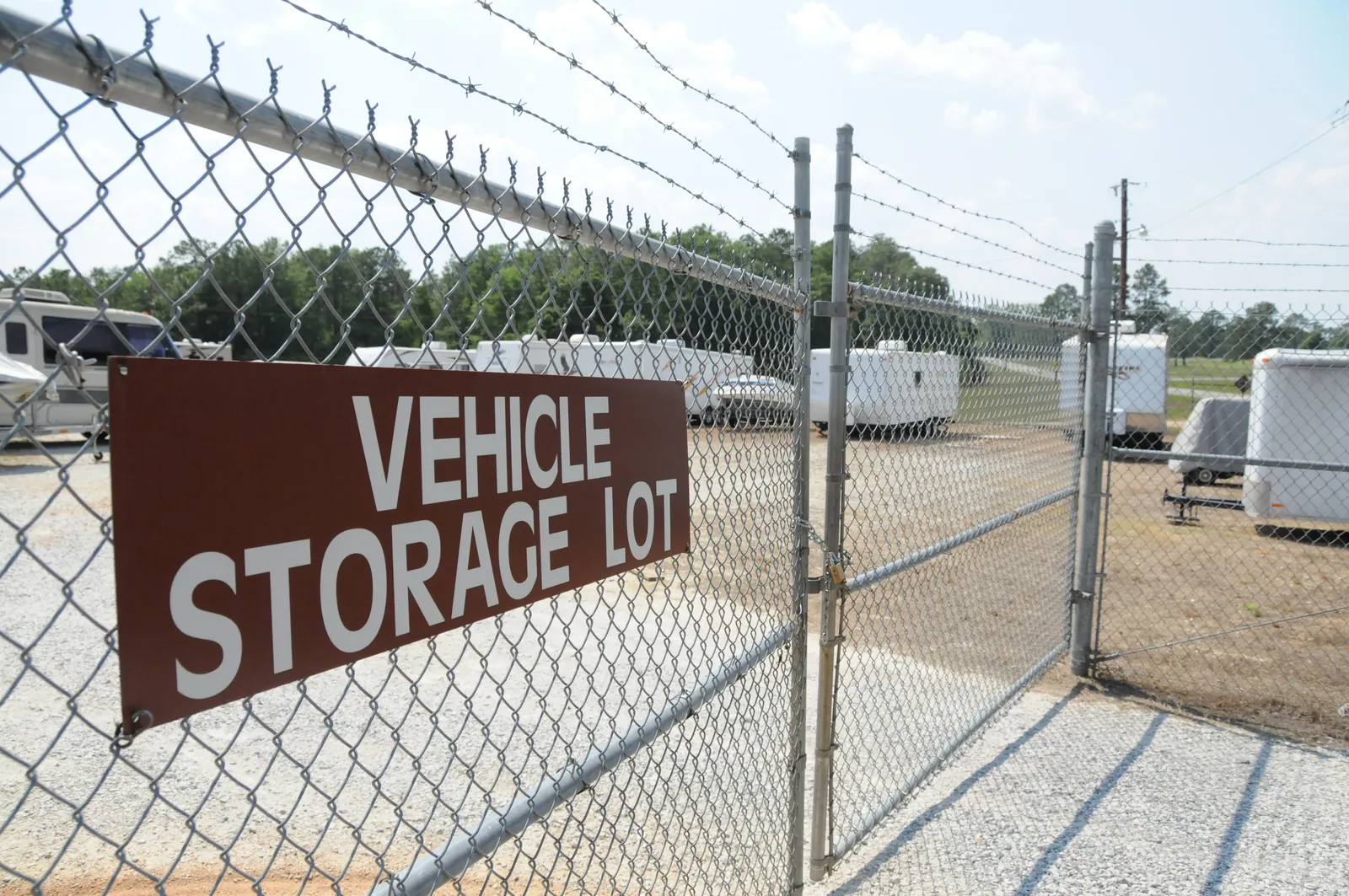 A fenced gravel vehicle storage lot with RVs and trailers behind a sign reading Vehicle Storage Lot
